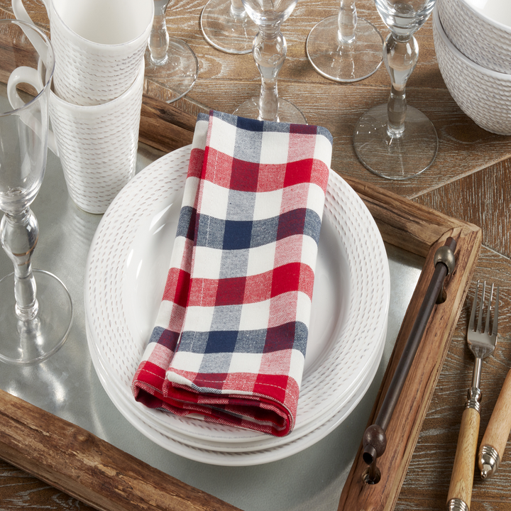 Set table with white plates, red and blue checkered napkin, and wooden cutlery on a wooden surface.
